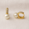 Clair Huggie Earrings, gold huggie hoop earrings with pavé-set surface and pearl drop detail, photographed on white linen background with soft editorial lighting.