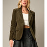 Model wearing the Cloe Corduroy Blazer Jacket in olive green featuring a tailored silhouette, notch lapels, single-button closure, flap pockets, and soft corduroy fabric, styled with a white crop top and black faux leather mini skirt.