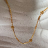 Colca Necklace by Matte, gold plated bar and bead chain with floral accents on ceramic surface