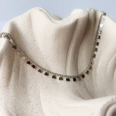 Dalia necklace gold plated heart charm chain on textured beige background
