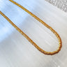 A gold-filled disc beaded necklace laid out on a surface, showcasing its layered and textured design on selenite background.