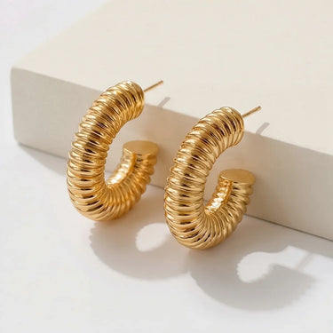 Angled view of Drake Hoop Earrings highlighting the polished gold-plated finish, evenly ribbed texture, rounded chunky silhouette, secure post-back closure, and reflective high-shine surface.