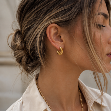 Model wearing Drake Hoop Earrings in polished gold plating, showcasing the chunky ribbed texture, sculptural rounded shape, lightweight fit, and bold everyday statement style.