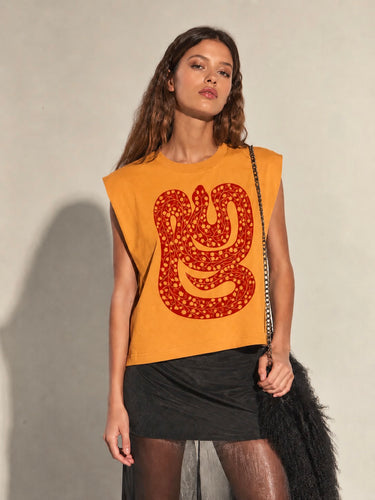 Model wearing the Drumar Graphic Tee in mustard yellow featuring the bold red snake graphic, crew neckline, structured cap sleeves, and relaxed cropped silhouette paired with black bottoms.