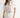 Woman wearing a white blouse with lace details on a plain background