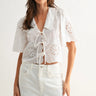 Woman wearing a white blouse with lace details on a plain background
