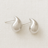 Felicia Stud Earrings in polished silver teardrop shape on beige linen background
