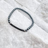 A stretch bracelet with black and white beads, displayed on a textured surface by Matte Jewelry