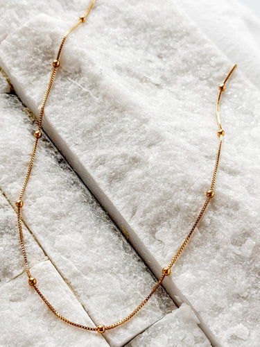 Follow gold plated beaded chain necklace by Matte, displayed on marble background