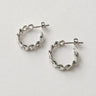 Genk Hoop Earrings featuring polished silver-plated hoop earrings with a braided chain-inspired texture, rounded hoop silhouette, mirror finish, secure hinged closure, lightweight design, and modern everyday style.
