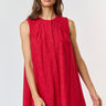 A woman wearing a vibrant red, sleeveless summer dress with a floral eyelet pattern, featuring a button-down front.