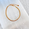 Gold disc bead bracelet with adjustable clasp on white textured surface.