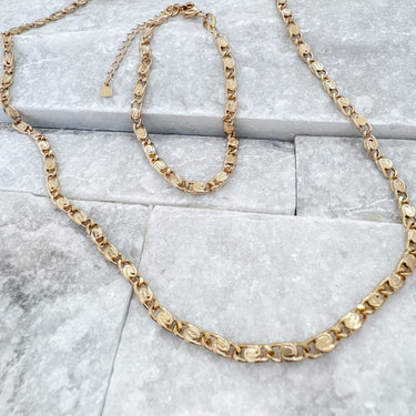 Gold chain link bracelet and matching necklace set displayed on gray stone background