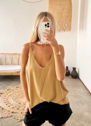 Model wearing the Terra Top in gold — silk V-neck tank, relaxed fit, paired with black shorts, minimalist resort look.