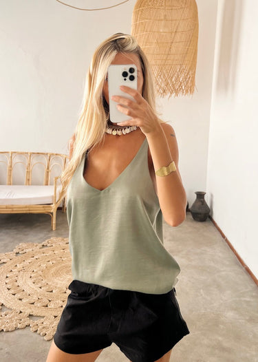 Model wearing the Terra Top in green— silk V-neck tank, relaxed fit, paired with black shorts, minimalist resort look.