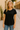 Model wearing the Gustavia T-Shirt — black cotton short-sleeve tee with classic round neckline, styled with jeans outdoors in natural light.