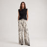 Woman wearing the black Harpenter ruffle blouse styled with printed wide-leg pants.