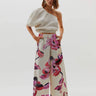 A model wearing floral print Hibiscus Pants with an elastic waistband and side pockets, paired with a beige spaghetti strap top.