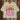 Humboldt Tee — white cotton t-shirt with vibrant retro sunset and cactus print in pink, orange, and purple tones, hanging on wooden background.