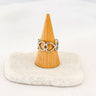 A gold-plated silver heart link ring displayed on a wooden stand with a white base.