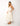 "side view of woman wearing ivory midi dress with gold star embroidery, v-neck, spaghetti straps, tiered skirt, tan sandals, summer resort style"