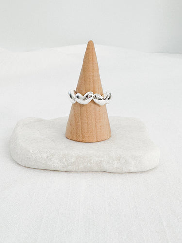 Silver-plated twisted heart sculptural ring displayed on wooden cone over marble base