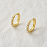 Josephine Huggie Earrings – small gold huggie hoop earrings with a slim polished finish, accented by a row of delicate white pearls, photographed on a soft neutral background.