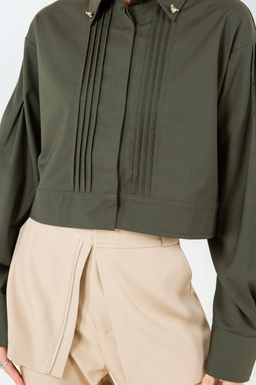 Olive green Kairo Blouse with structured pintucks and modern cropped fit, styled with beige tailored trousers on a bright white backdrop, close up.