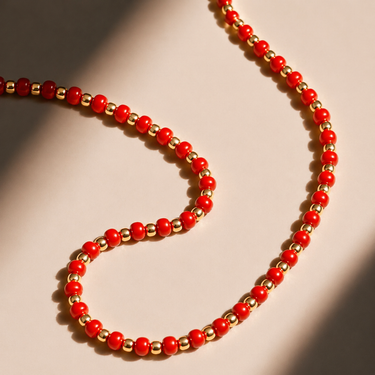 Kip Necklace close-up of red beaded chain with gold accents on neutral background, highlighting color contrast and polished finish.