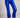 Model wearing cobalt blue slim pants with coated finish and white top — modern city look.
