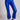 Model wearing cobalt blue slim pants with coated finish and white top — modern city look.
