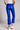 Model wearing cobalt blue slim pants with coated finish and white top — modern city look, back view.