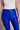 Model wearing cobalt blue slim pants with coated finish and white top — modern city look.
