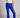 Model wearing cobalt blue slim pants with coated finish and white top — modern city look.
