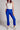 Model wearing cobalt blue slim pants with coated finish and white top — modern city look.
