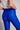 Model wearing cobalt blue slim pants with coated finish and white top — modern city look close up back view.