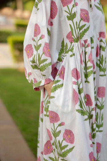 Woman wearing Lissandra Maxi Dress with pink and green floral print walking outdoors in garden setting.