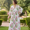 Woman wearing Lissandra Maxi Dress with pink and green floral print walking outdoors in garden setting.