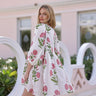 Model wearing white mini dress with pink floral print and long sleeves, resort style.