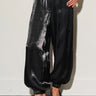 Woman wearing Lumit black balloon pants featuring a relaxed silhouette, elastic waistband, gathered ankle hem, and a lustrous finish.