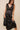 Model wearing Maira Asymmetrical Dress in black satin, showing sleeveless fit and asymmetrical hem.