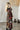 Woman wearing Managua Dress in black tropical print with slit, standing in a minimal neutral interior.