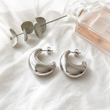 Close-up of Marina Hoop Earrings showcasing the polished mirror finish, sculptural crescent silhouette, smooth curved profile, secure post-back closure, and contemporary statement design.