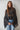 Woman wearing the Maruk Blouse in black, featuring a lightweight sheer fabric, relaxed silhouette, elegant high neckline, dramatic tiered bell sleeves, and flowing design styled with blue denim jeans.
