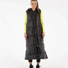 Front view of woman wearing long black hooded puffer vest with quilted design.