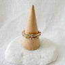 A gold-filled pave ring with a snake design displayed on a beige cone-shaped stand against a white background.