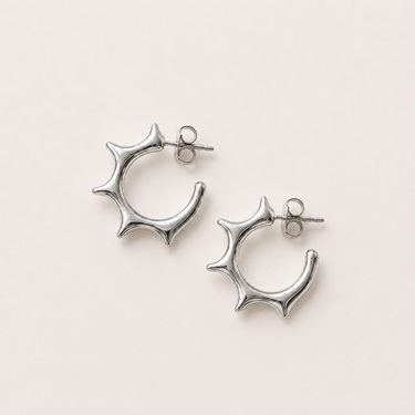 Millan Hoop Earrings featuring polished silver-plated hoop earrings with sculptural starburst edges, a rounded open-hoop silhouette, smooth mirror finish, secure post-back closure, lightweight design, and modern statement style.