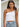 Model wearing the Minuett Top in white featuring a fitted ribbed knit construction, asymmetrical one-shoulder neckline, and cropped silhouette, paired with light-wash denim jeans.