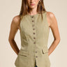 Model wearing the Muse Vest in soft sage green featuring a tailored fitted silhouette, button-front closure, pointed hem, sleeveless cut, and decorative flap pockets paired with light wash denim jeans.