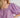 A woman wearing a purple blouse with short puffed sleeves and lace detailing around the neck.